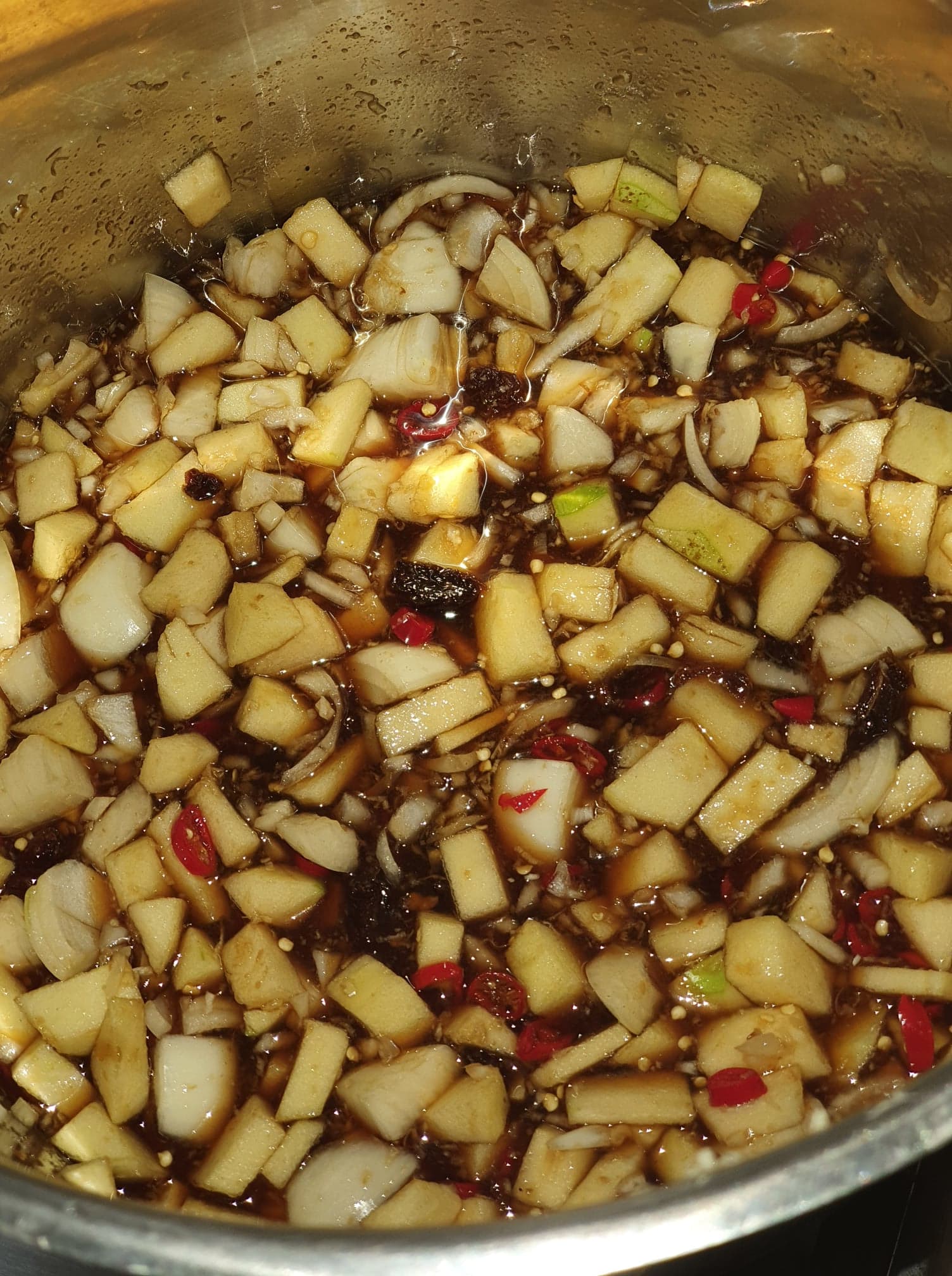 A large pot of mango chutney simmering on a stove, steam rising and a wooden spoon resting on the rim